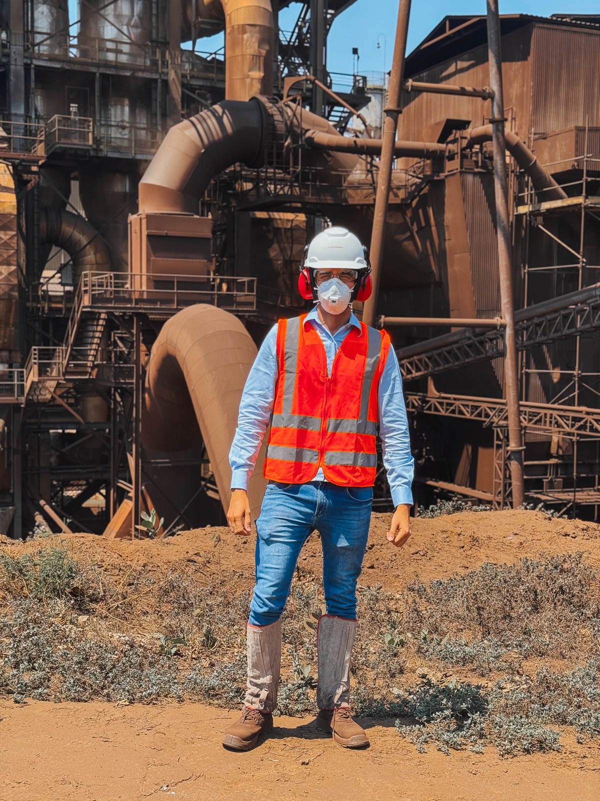 Profissional com equipamentos de proteção individual diante de uma unidade de processamento mineral
